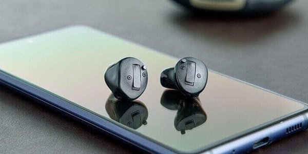 Aparaty słuchowe Oticon Own™ leżące na ekranie smartfona.