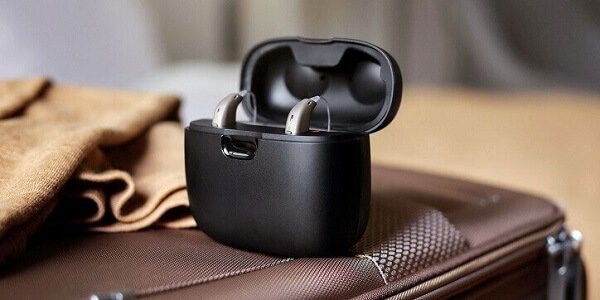 Aparaty słuchowe Oticon Real™ w etui ładującym na walizce.