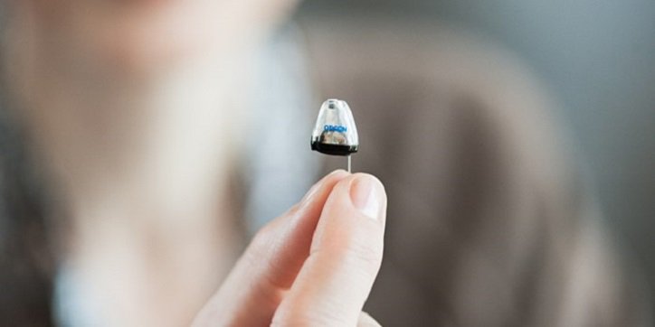 Kobieta trzyma dyskretny aparat słuchowy w Centrum Słuchu Audika.