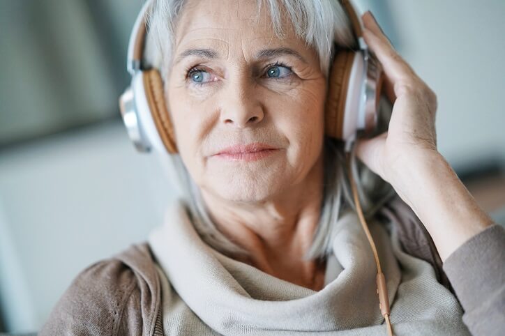 Kobieta w średnim wieku podczas badania słuchu w gabinecie audiologa, nosząca słuchawki i koncentrująca się na testach dźwiękowych.
