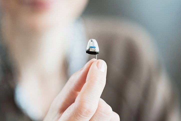 Niewidoczny aparat słuchowy trzymany między palcami, idealny dla osób ceniących dyskrecję i zaawansowaną technologię słyszenia.