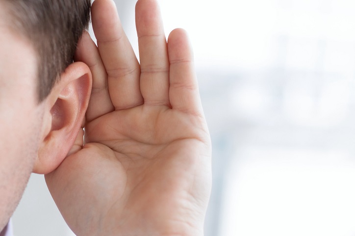 Mężczyzna przykłada dłoń do ucha, nasłuchując dźwięków.