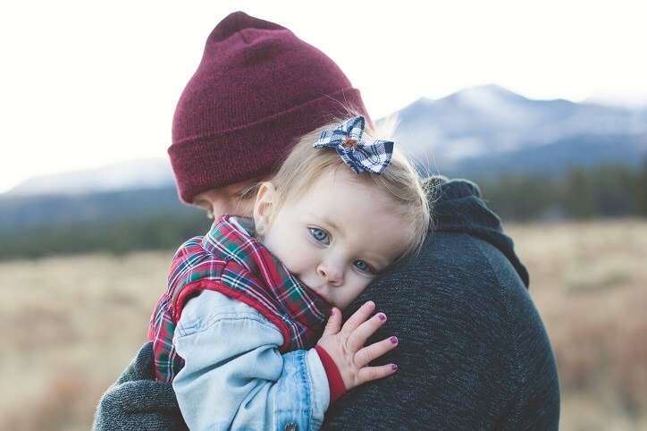 Ojciec przytula dziecko na tle gór, zauważając pierwsze objawy problemów ze słuchem.