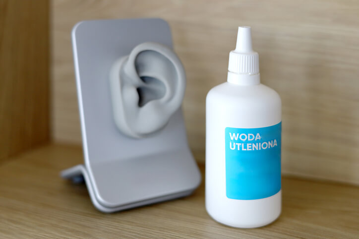 Woda utleniona w butelce z aplikatorem obok modelu ucha na drewnianej powierzchni.