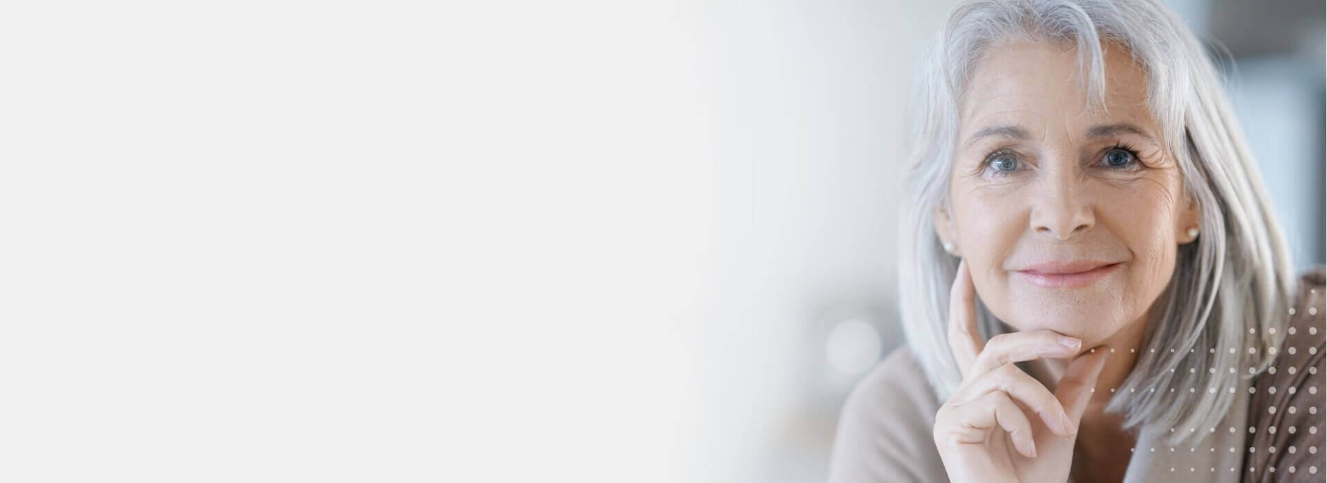 Starsza kobieta z siwymi włosami nosi aparaty słuchowe i delikatnie się uśmiecha.