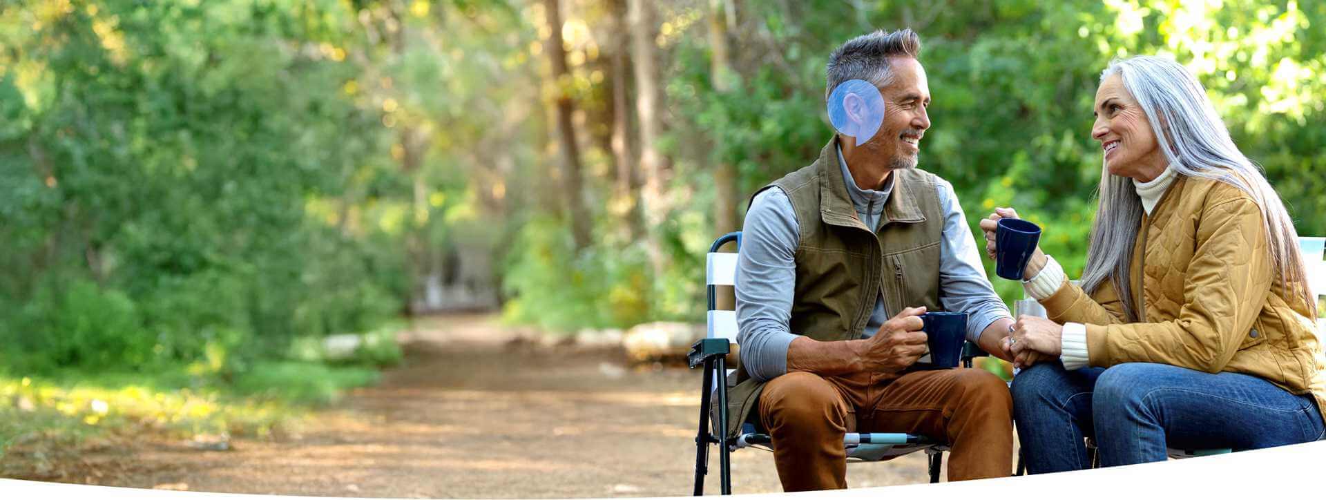 Osoby starsze rozmawiające na łonie natury, trzymając kubki, symbolizujące korzyści z leczenia ubytku słuchu w Audika.