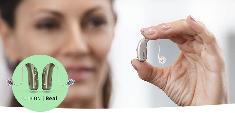 Ręka trzyma aparat słuchowy marki Oticon, delikatny i nowoczesny model douszny, w jasnym, neutralnym otoczeniu, co sugeruje profesjonalną klinikę słuchu, np. Audika.