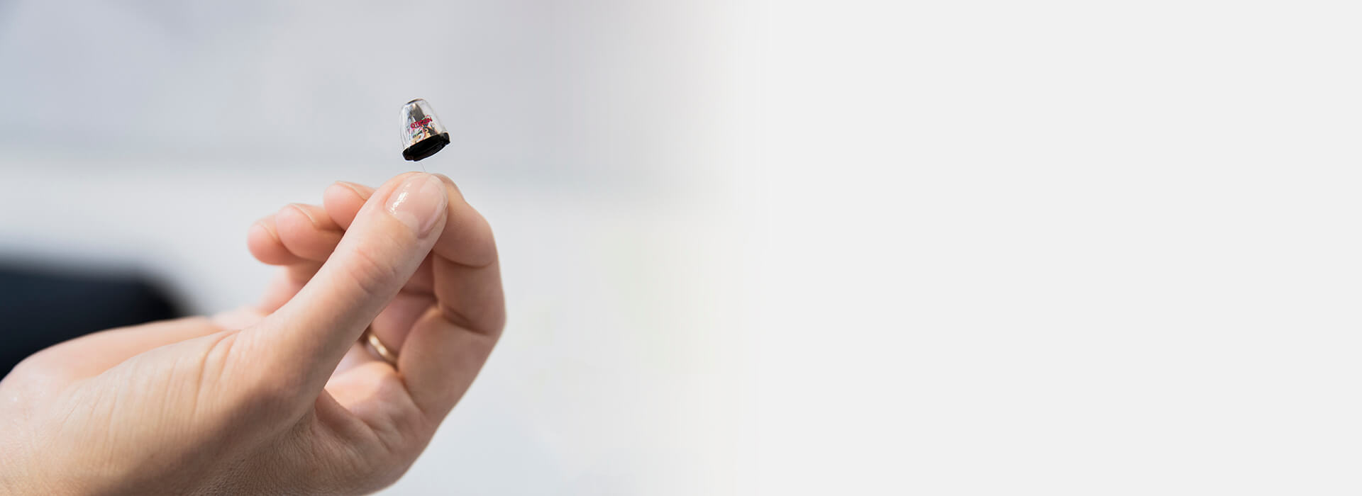 Ręka trzymająca niemal niewidoczny aparat słuchowy.