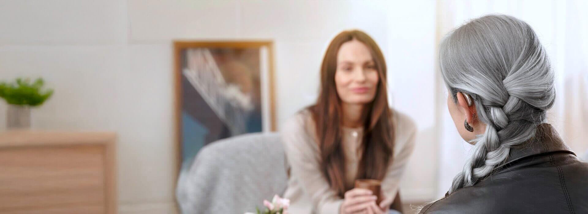 Kobieta z aparatem słuchowym Oticon Intent™ rozmawia z doradcą w jasnym, przytulnym wnętrzu.
