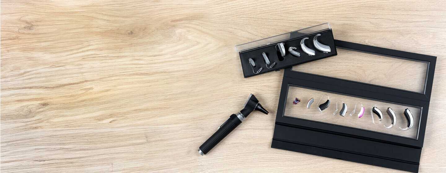 Różne typy aparatów słuchowych z akcesoriami na drewnianym blacie.