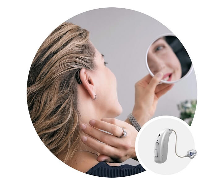 Kobieta zakłada zauszny aparat słuchowy BTE, patrząc w lusterko w domu.