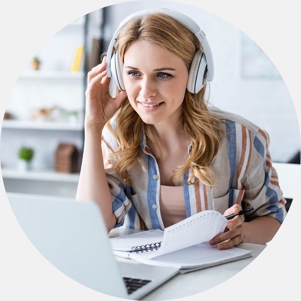 Specjalista Audika w słuchawkach uczestniczy w szkoleniu online, robiąc notatki.