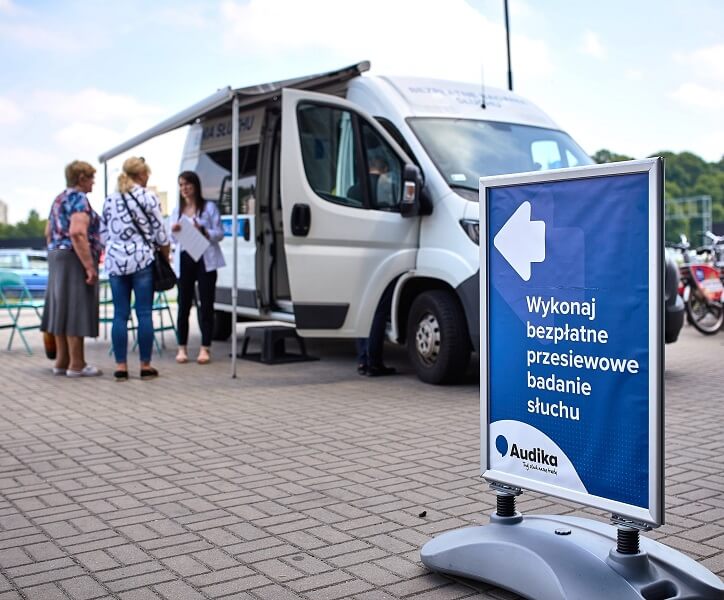 Mobilny gabinet Audika z tablicą informacyjną o bezpłatnych badaniach słuchu.
