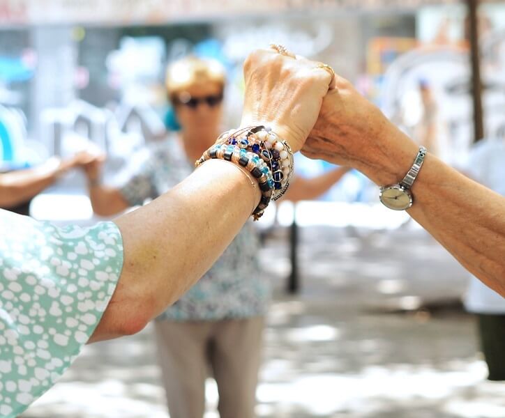 Starsze osoby trzymające się za ręce podczas wspólnej aktywności na świeżym powietrzu.