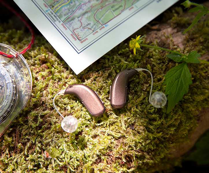 Aparaty słuchowe na mchu obok mapy i kompasu, idealne do aktywności na świeżym powietrzu.