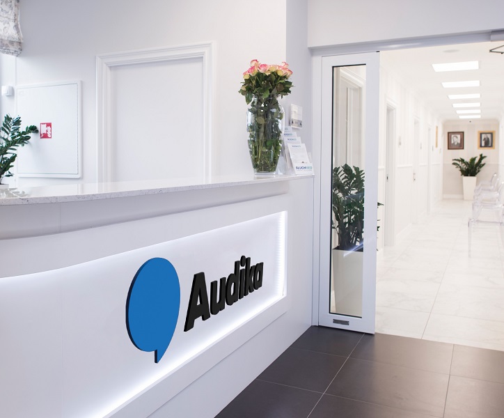 Nowoczesna recepcja w Centrum Medycznym Audika z logo na ladzie, bukietem róż i jasnym, eleganckim wnętrzem w tle.