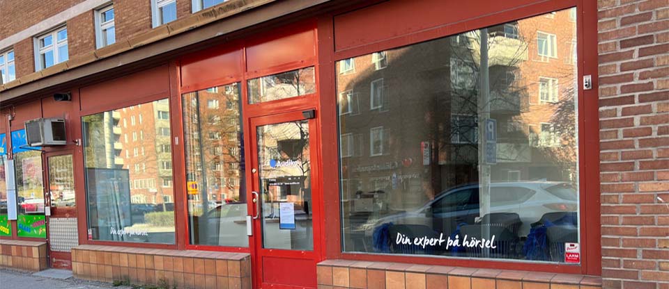  Entrén till Audikas hörselklinik i Huddinge med texten ’Din expert på hörsel’ på skyltfönstret.