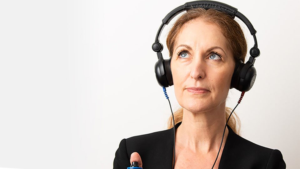  Kvinna med hörlurar gör gratis hörselkoll hos Audika och får en indikation på sin hörsel.