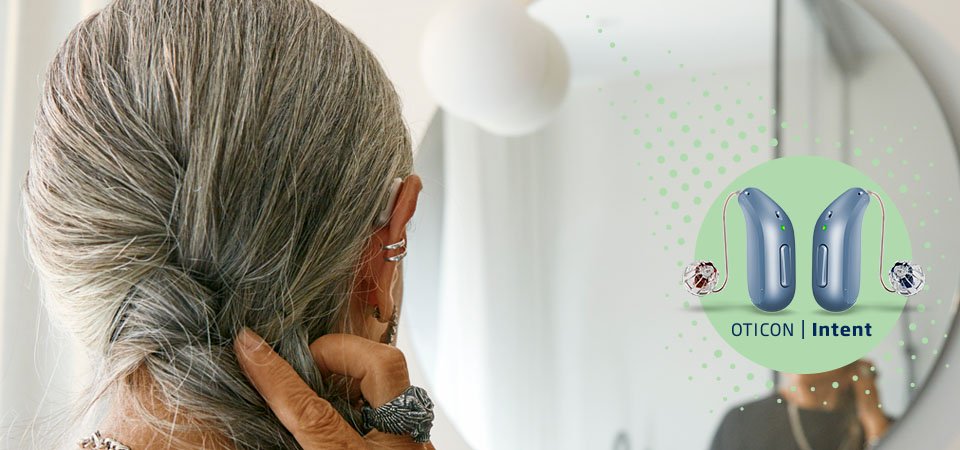  Kvinna med grått hår som bär Oticon Intent-hörapparat, en nyhet hos Audika.