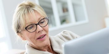  Äldre kvinna använder en iPad i en ljus hemmiljö.