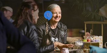  Kvinna med hörapparat samtalar och skrattar med en vän över en fika.