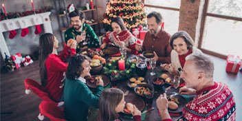  En familj som sitter runt ett festligt dukat bord och samtalar, stärkta av kommunikationstips från Audika.