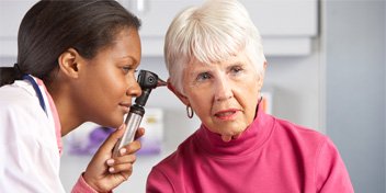  Audionom undersöker en äldre kvinnas öra för att identifiera eventuell hörselnedsättning under en hörselscreening.