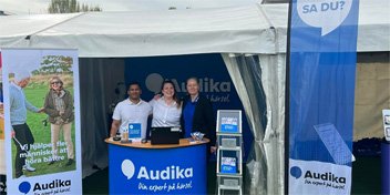  Tre medarbetare från Audika vid en seniormässa som pratar om hörsel och erbjuder snabbtest av hörseln framför en informationsmonter.