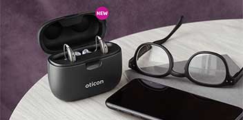  Smartcharger laddstation från Oticon tillsammans med glasögon och en mobiltelefon på ett bord