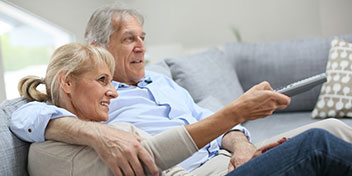  Par använder hörselhjälpmedel för att titta på tv tillsammans och håller i en fjärrkontroll.