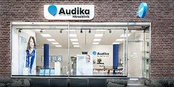  Audikas hörselklinik med glasfasad och varumärkesskylt på byggnadens framsida.