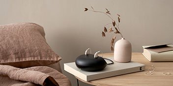  Avancerade hörapparater som laddas i en laddningsstation på ett stilrent nattduksbord.