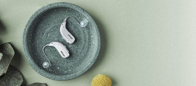  Nya hörapparater i silver placerade på ett runt fat, tillgängliga för utprovning.