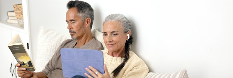 Man och kvinna sitter i soffan, kvinnan använder surfplatta för att genomföra ett hörseltest online.