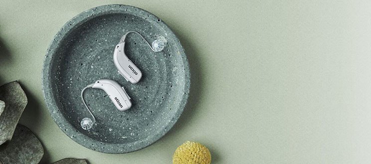  Nya hörapparater i silver placerade på ett runt fat, tillgängliga för utprovning.