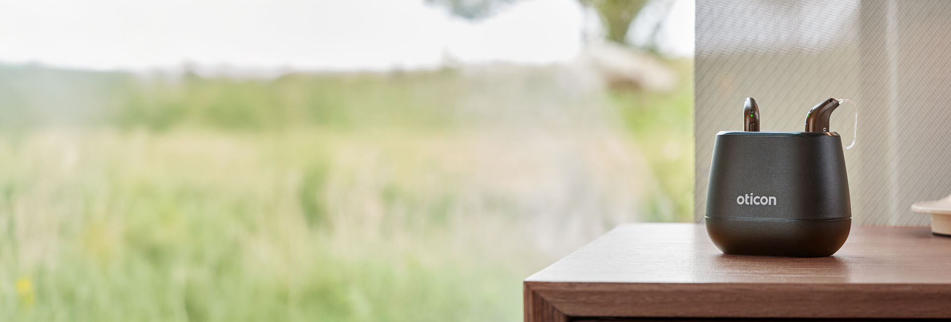 En uppladdningsbar hörapparat med laddstation som står på ett bord 