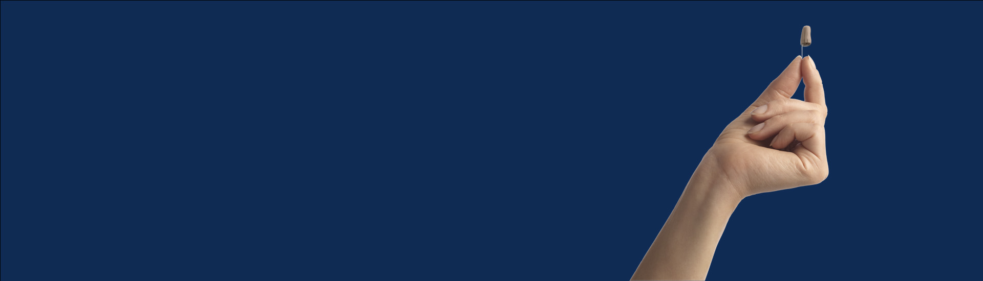 Bild på en hand som håller upp en allt-i-örat hörapparat som du kan testa hos Audika