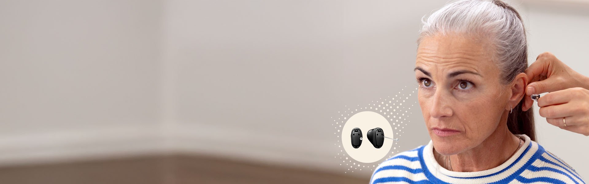  En person får en hörapparat justerad av en audionom i en ljus klinikmiljö. Ikonvisning inkluderar två svarta hörapparater. Kontext kopplad till hörselvård och hörselhjälpmedel.
