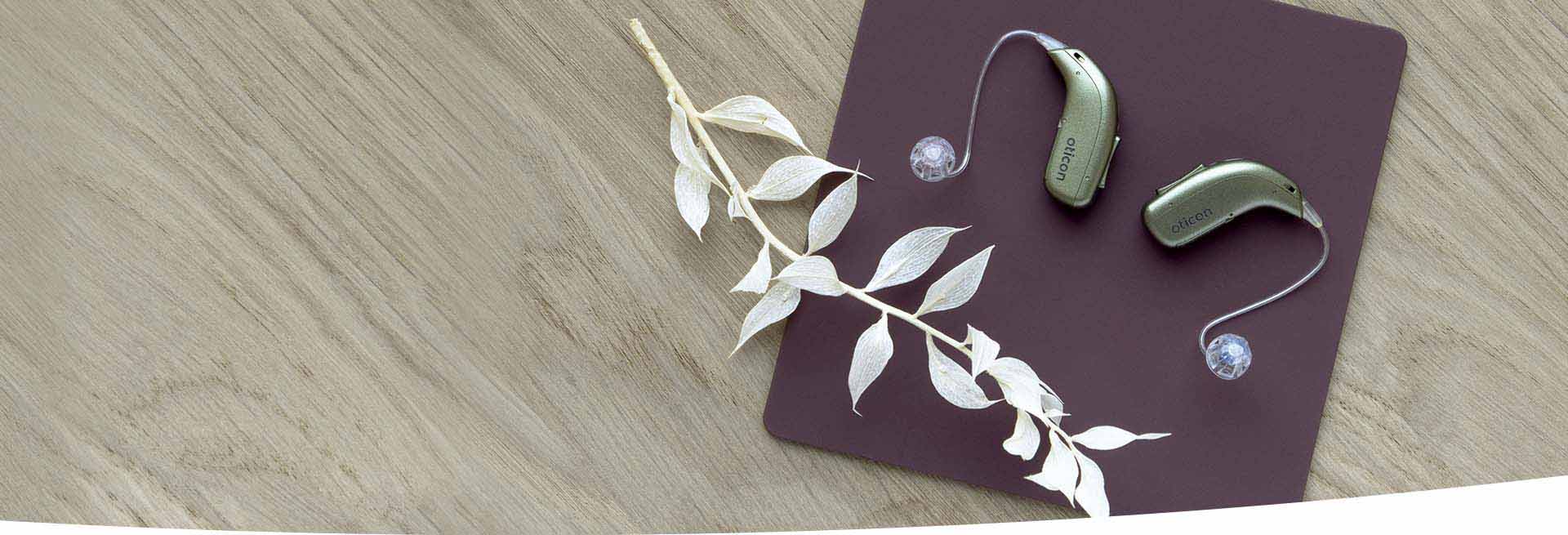  Hörapparaten Oticon Real på ett brunt underlag, tillgänglig för 30 dagars test hos Audika.