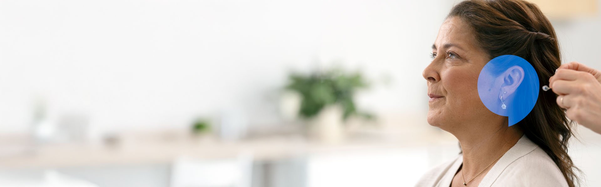  Kvinna som testar en hörapparat hos Audika. Över hennes öra är en blå pratbubbla.