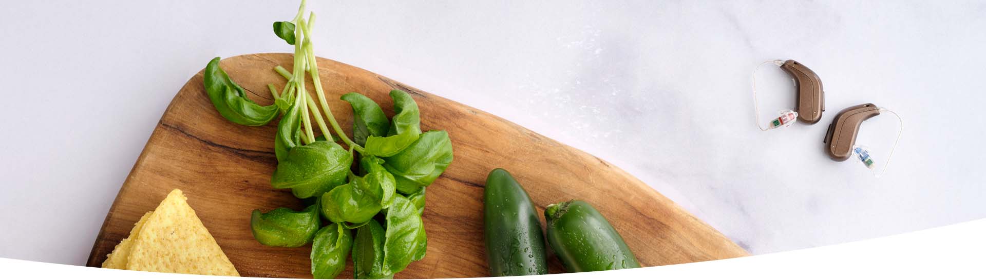  Hörapparater bredvid färska örter och grönsaker på en träskärbräda.