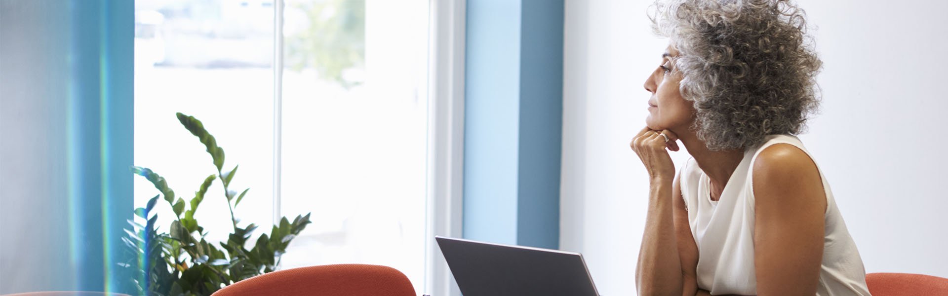  Kvinna med hörapparater som lindrar tinnitus, sitter vid en laptop och tittar ut genom ett fönster.