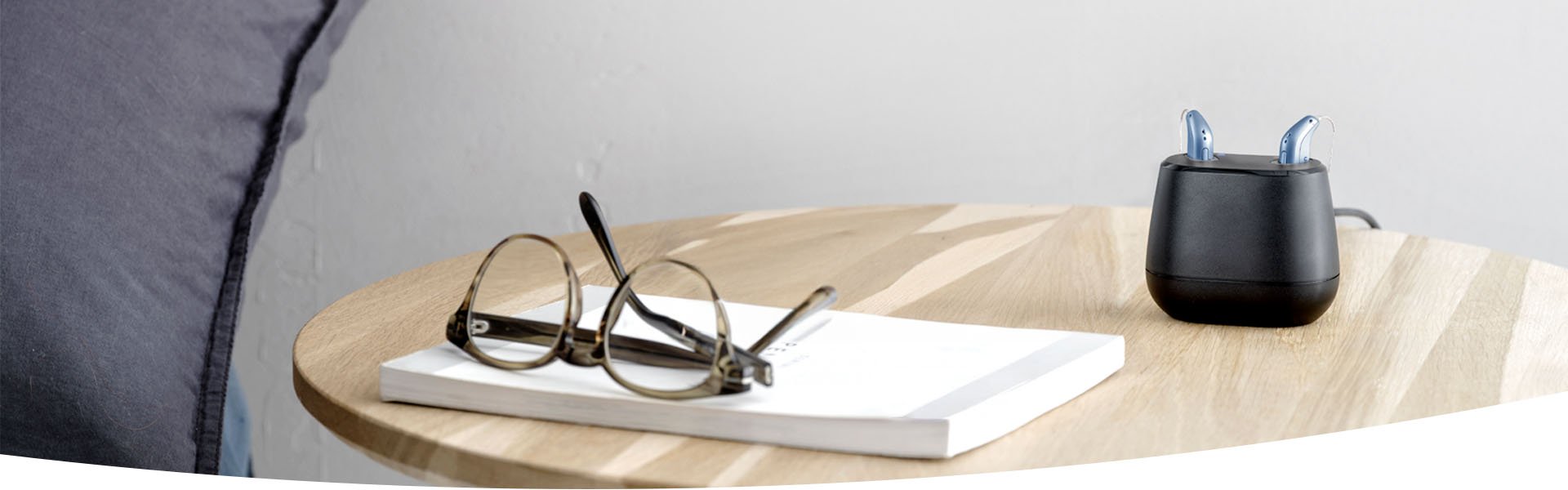  Laddstation för uppladdningsbara hörapparater på ett bord bredvid glasögon och en bok