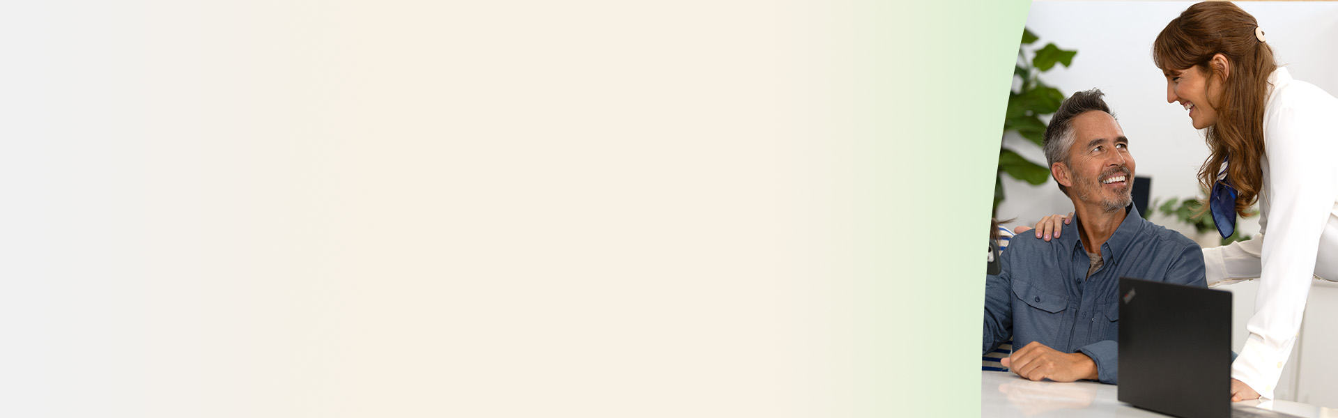  En audiolog i vit rock hjälper en man under ett hörseltest vid en dator i en ljus och professionell hörselklinik med gröna växter i bakgrunden.