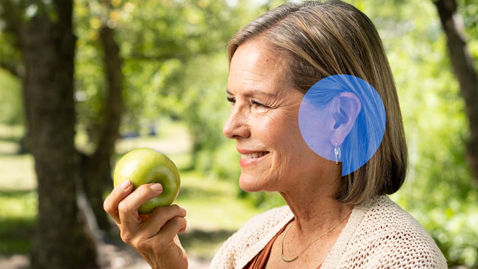 Kvinna som har en hörselnedsättning och bär en hörapparat som står i en trädgård
