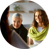  Två personer sitter hos audionom vid ett bord i en ljus miljö med suddiga ansikten, sett från en tredje persons perspektiv. Väggmonterade hyllor och växter skymtar i bakgrunden. 