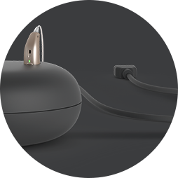 Bild på laddare till laddningsbara hörapparater som är ansluten till eluttag med integrerad kabel.