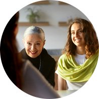  Två personer sitter hos audionom vid ett bord i en ljus miljö med suddiga ansikten, sett från en tredje persons perspektiv. Väggmonterade hyllor och växter skymtar i bakgrunden. 