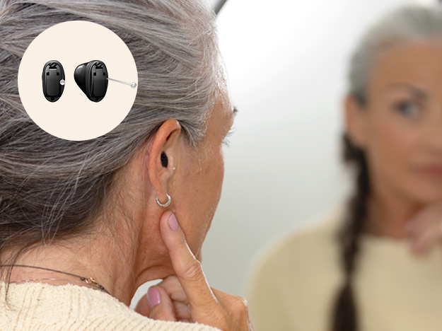 Kvinna som tittar sig i spegeln och hörapparaten Oticon Own Si i örat
