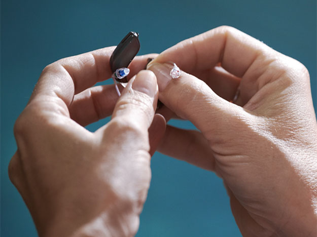 Bild på två händer som byter tillbehör på en hörapparat under öppen mottagning på Audika